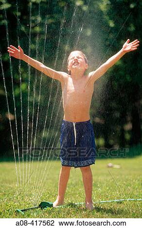 Stock Image - Spirited boy gets wet from sprinkler on a hot summer day. Pennsylvania, USA. Fotosearch