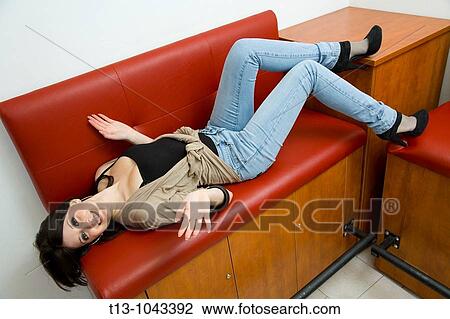 Stock Image - Spreading on a Red sofa attractive young woman. Fotosearch