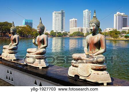 Stock Image - Sri Lanka - Capital City Colombo, Buddha Statues in Seema Malaka Temple on Beira Lake, ´World Trade Center´ in the background, Sri Lanka, Asia. Fotosearch