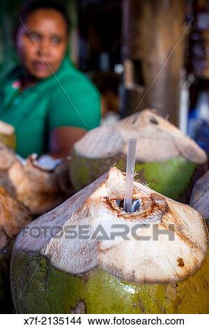 Picture - stall, woman selling green coconut to drink its water, in Bibijagua beach, Punta Cana, Dominican Republic.. Fotosearch