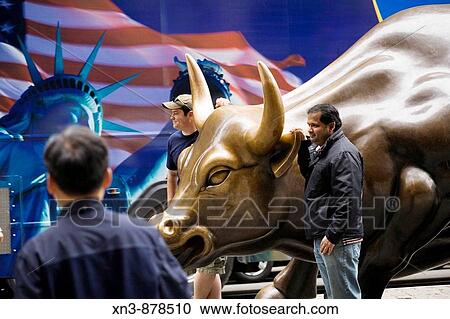 Stock Image - Standing by bronze statue of charging bull, Bowling Green park, Wall Street, New York, USA. Fotosearch