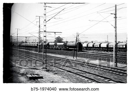 Stock Image - Station with trains, vagons, train tracks and telecommunications and electricity towers seen through the window of a train. Fotosearch