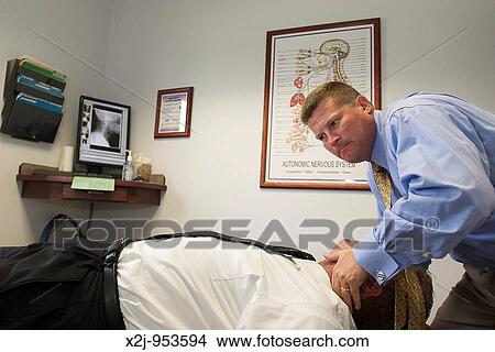 Picture - Sterling Heights, Michigan - Dr William F Goss does an adjustment for a patient in his chiropractic clinic. Fotosearch