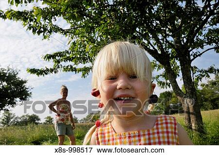 Stock Photo - Stock photo of a 3 year old girl picking cherries with her mum She is wearing cherries for earings. Fotosearch