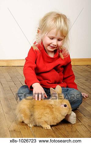 Stock Image - Stock photo of a four year old girl playing with her pet rabbits on a wooden floor. Fotosearch