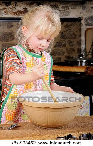 Stock Image - Stock photo of a four year old girl using a wodden spoon to mix up some cookie dough to make biscuits. Fotosearch