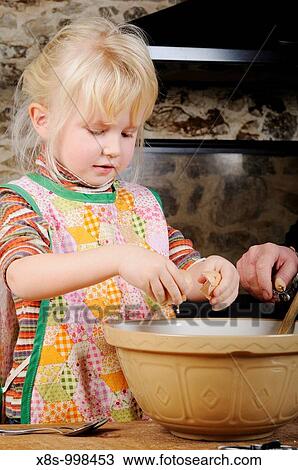 Stock Image - Stock photo of a four year old girl cracking eggs into a mixing bowl ready to make some cookies. Fotosearch