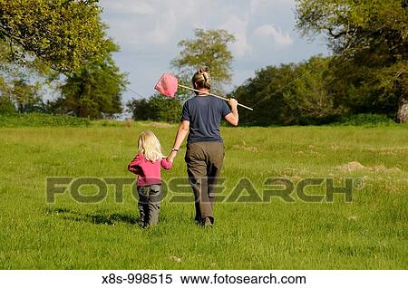 Stock Photography - Stock photo of a mother and her 3 year old daughter walking hand in hand across a field as they go on a fishing trip. Fotosearch