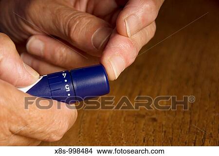 Picture - Stock photo of a seventy year old woman performing a test for her blood glucose levels to monitor her diabetes The image shows the woman using an accu-check Aviva testing system. Fotosearch
