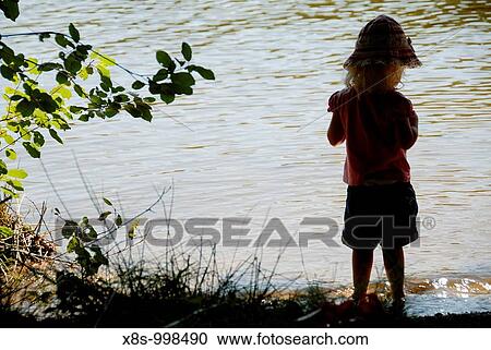 Stock Image - Stock photo of a two year old girl standing in the water at the waters edge The image shows the girl in partial silouhette and captures the dreamy quality of childhood. Fotosearch