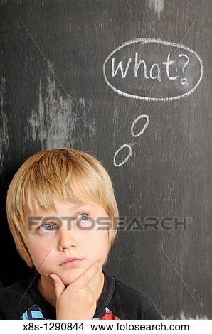 Picture - Stock photo of a young boy in fornt of a blackboard with chalk thought bubbles spelling the word What. Fotosearch
