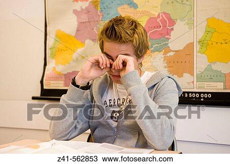 Stock Image - Student weeping his eyes in the classroom. Fotosearch
