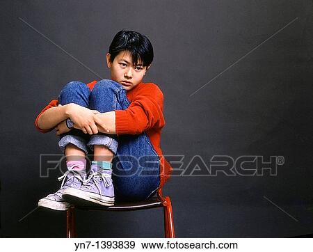 Studio image of a an Asian teenage girl sitting on a chair clasping her knees and looking forlorn View Large Photo Image Stock Photo - Studio image of a an Asian teenage girl sitting on a chair clasping her knees and looking forlorn. Fotosearch