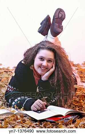 Stock Image - studio image of teenage girl lying in the autumn leaves smiling at the camera. Fotosearch