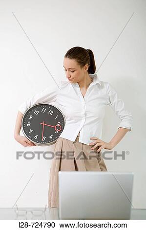 Stock Image - Studio portrait of young businesswoman holding clock. Fotosearch