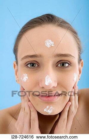 Stock Photograph - Studio portrait of young woman with moisturizer on cheek, close-up. Fotosearch