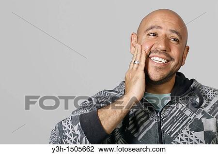 Stock Image - Studio shot of Mexican man, hand on cheek. Fotosearch