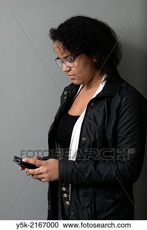 Studio Tuinstraat, Tilburg, Netherlands. Studio-portrait of a young, Caribbean woman, using her smartphone to monitor social media. View Large Photo Image Stock Image - Studio Tuinstraat, Tilburg, Netherlands. Studio-portrait of a young, Caribbean woman, using her smartphone to monitor social media.. Fotosearch
