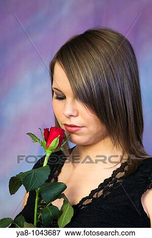 Stock Photo - Studio, UK, Europe Young woman smelling a red rose. Fotosearch