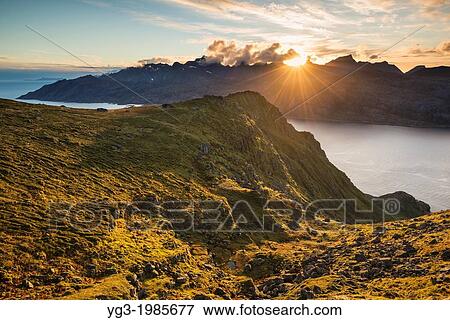 Stock Photo - Sun setting behind mountains of Flakstadoy from Skottind, Vestv? goya, Lofoten islands, Norway. Fotosearch