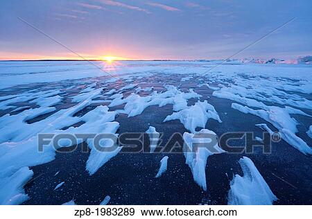 Stock Photo - Sun setting over a frozen lake in Ontario, Canada.. Fotosearch