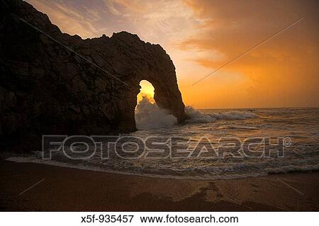 Sun setting through Durdle Door during rough weather and stormy Sea. View Large Photo Image Stock Photo - Sun setting through Durdle Door during rough weather and stormy Sea.. Fotosearch