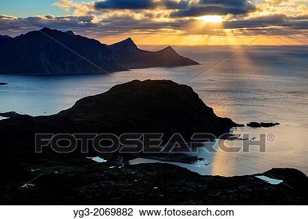 Stock Image - Sun shines low over sea from summit of Holandsmelen, Vestvagoy, Lofoten Islands, Norway.. Fotosearch