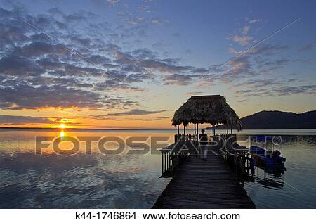 Picture - Sunset at dock in the shores of Lake Pet? n Itza, with Cerro Cahu? in the background, Peten, Guatemala. Fotosearch
