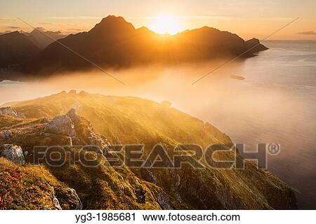 Stock Image - Sunset behind mountains from summit of Offersoykammen, Vestvagoya, Lofoten Islands, Norway.. Fotosearch