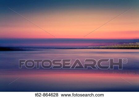 Stock Photo - Sunset from the sea with the city lights in the background Long exposure. Fotosearch