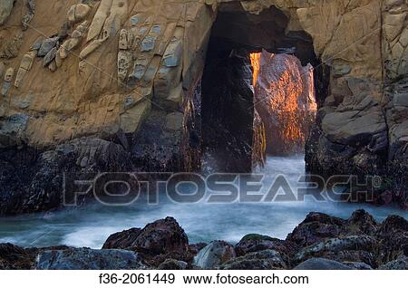 Stock Photo - Sunset light and waves coming through hole in coastal rock at Pfeiffer Beach, Big Sur, California.. Fotosearch