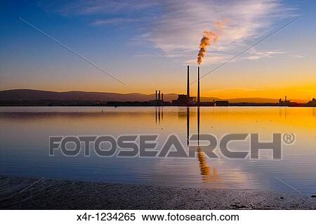 Stock Photography - Sunset over Dublin Bay, Ireland. To the right is the iconic Poolbeg Power Station, with smoke billowing from its right cooling tower. Fotosearch