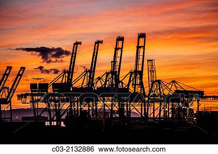 Stock Photograph - Sunset silhouettes container cargo loading cranes in the Port of Long Beach, CA.. Fotosearch