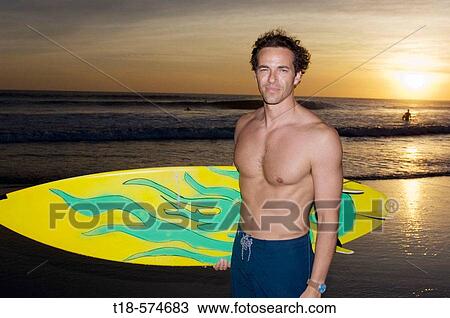 surfer posing on beach with sunset in the background View Large Photo Image Stock Image - surfer posing on beach with sunset in the background. Fotosearch