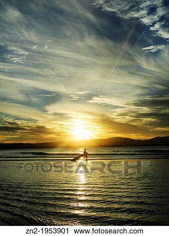Stock Image - surfers in the sunset, Byron Bay, Australia.. Fotosearch