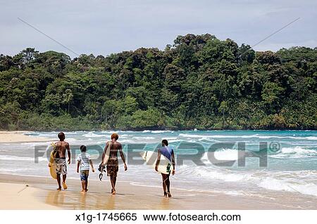 Stock Photography - Surfers walking along the sea at Wizard Beach First Beach on Isla Bastimentos, Bocas del Toro, Panama. Fotosearch