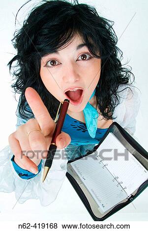 Surprise brunette taking pen in hand indicates with her finger towards the camera in the other hand has a calendar with appointments View Large Photo Image Stock Photo - Surprise brunette taking pen in hand indicates with her finger towards the camera in the other hand has a calendar with appointments. Fotosearch