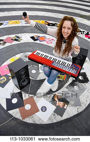 Stock Image - Surrounded with longplay records with a microphone in hand. Fotosearch