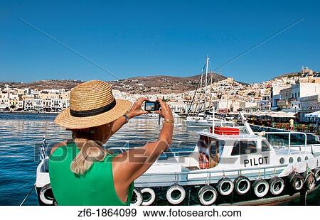 Syros Greece Islands in Hermoupolis capital in marina harbor boats ships port white buildings water boating fishing architecture with tourist lady in green with camera taking pictures View Large Photo Image Stock Photo - Syros Greece Islands in Hermoupolis capital in marina harbor boats ships port white buildings water boating fishing architecture with tourist lady in green with camera taking pictures. Fotosearch