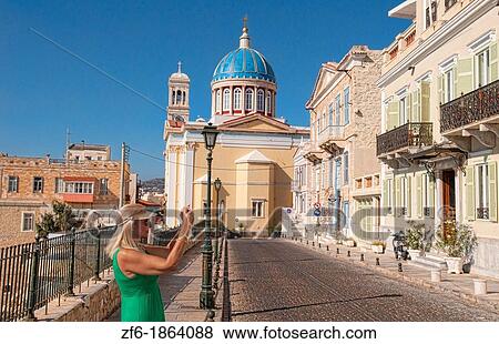 Stock Photo - Syros Greece Islands with tourist and camera woman in Hermoupolis capital white buildings and church St Nicholas Cathedral at blue dome and classic architecture. Fotosearch