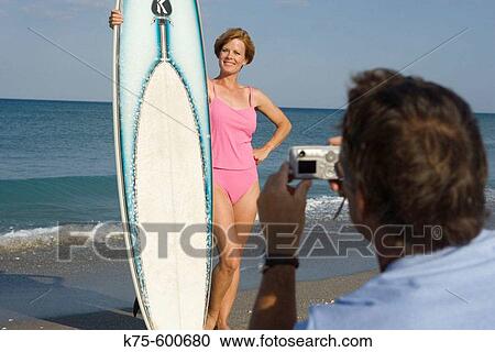 Stock Image - Taking a picture of a woman with her surfboard. Fotosearch