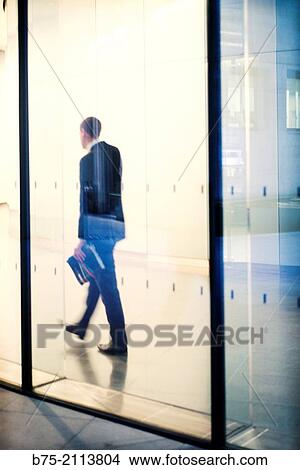 Talking on phone in an office corridor, seen through a glass in the City of London, England, UK, Europe unrecognizable with a folder in hand Executive. View Large Photo Image Picture - Talking on phone in an office corridor, seen through a glass in the City of London, England, UK, Europe unrecognizable with a folder in hand Executive.. Fotosearch