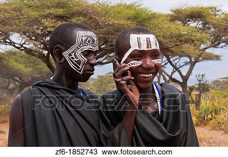 Stock Image - Tanzania Serengeti Africa Masai Maasai boys talking on cell phone in black clothes from circumcision ceremony with face paint 7. Fotosearch