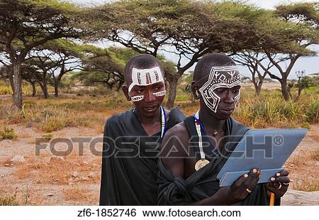 Tanzania Serengeti Africa Masai Maasai boys playing with Digital tablet computer in black clothes from circumcision ceremony with face paint 7 View Large Photo Image Stock Photograph - Tanzania Serengeti Africa Masai Maasai boys playing with Digital tablet computer in black clothes from circumcision ceremony with face paint 7. Fotosearch