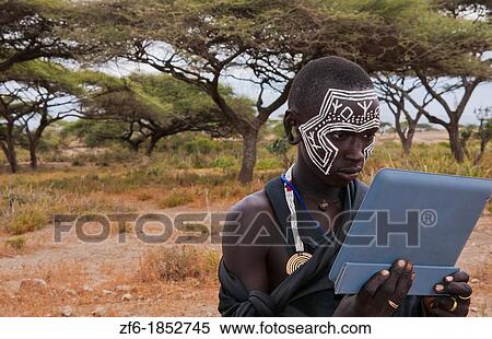 Tanzania Serengeti Africa Masai Maasai boy playing with Digital tablet computer in black clothes from circumcision ceremony with face paint 7 View Large Photo Image Stock Photography - Tanzania Serengeti Africa Masai Maasai boy playing with Digital tablet computer in black clothes from circumcision ceremony with face paint 7. Fotosearch
