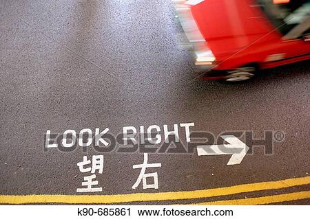 Stock Image - Taxi moving on the street with warning sign in english and chinese writing on the asphalt, indicating to pay attention before crossing the road, Hong Kong Island, Hong Kong, PR China, East Asia. Fotosearch