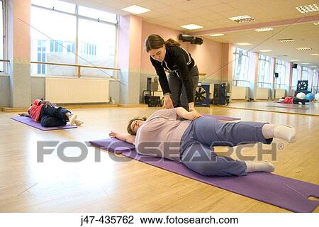 Stock Image - Teacher correcting the position of a lady doing pilates. Fotosearch