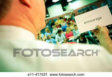 Stock Image - Teacher holding? Encourage? sign in a college classroom.. Fotosearch