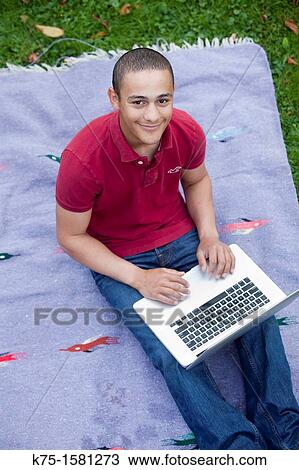 Stock Image - Teen boy studying with laptop outdoors. Fotosearch