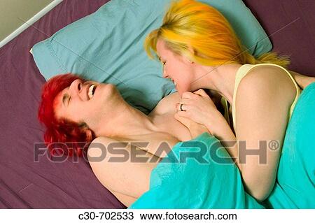 Stock Image - Teen boy, with dyed red hair, and his blond girl friend lying together in bed. Fotosearch